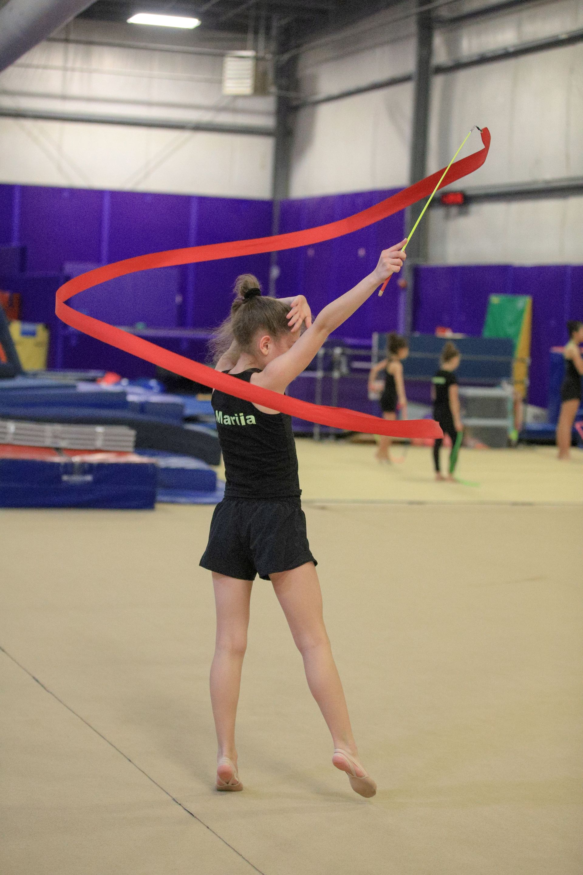 A young girl is practicing rhythmic gymnastics with a red ribbon