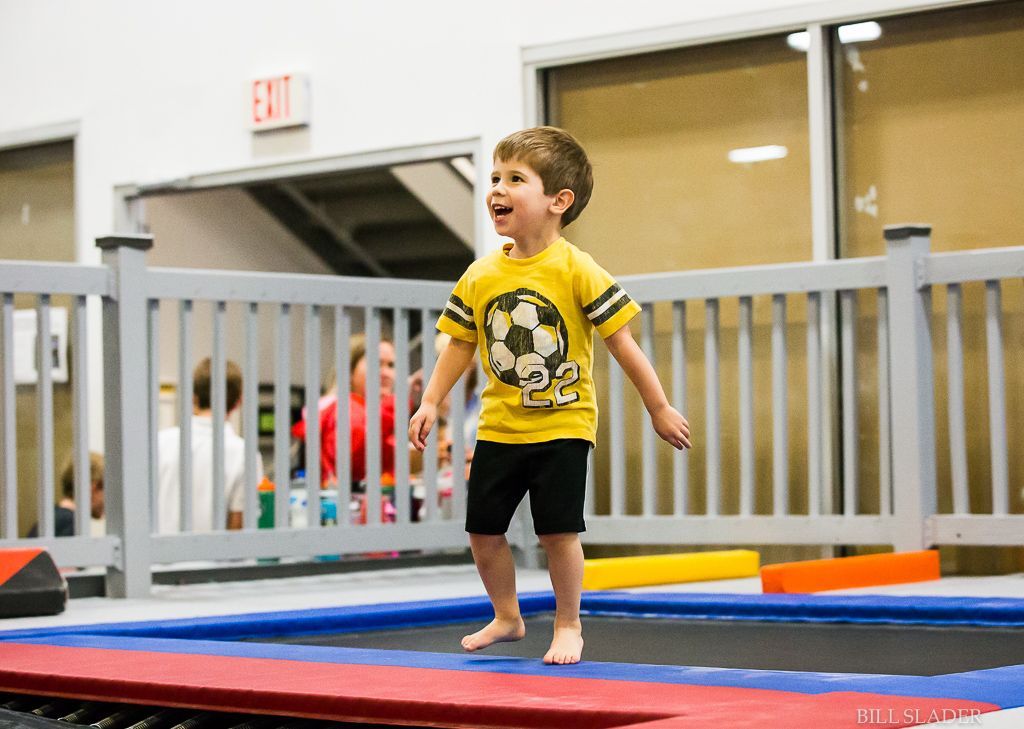 A young boy in a yellow shirt is jumping on a trampoline.