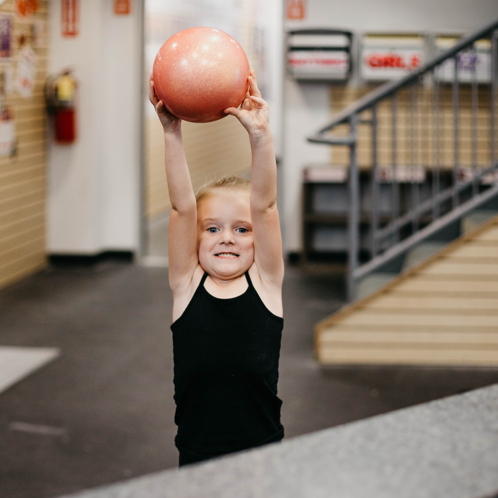 A little girl is holding a ball over her head