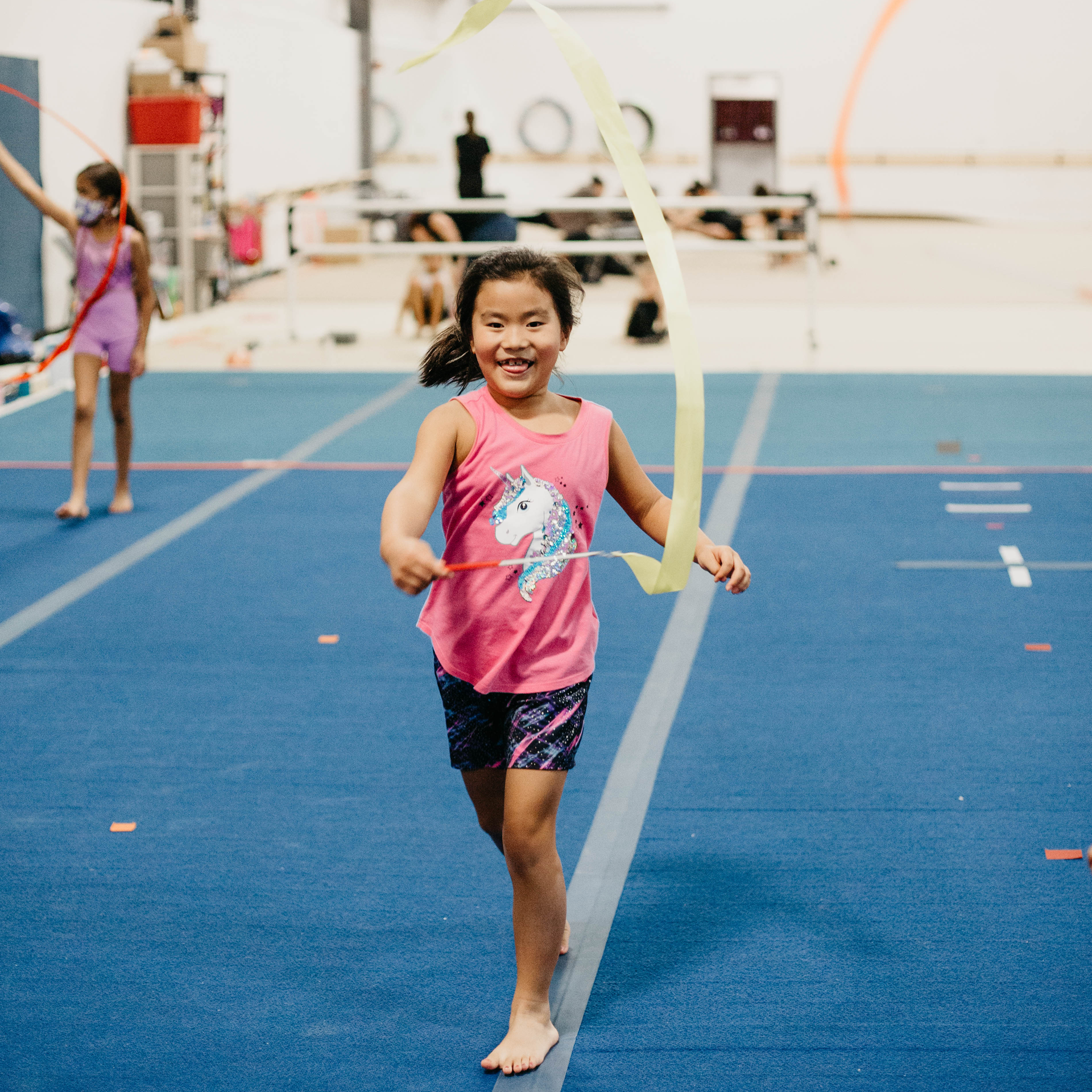 A little girl in a pink tank top with a unicorn on it is holding a ribbon