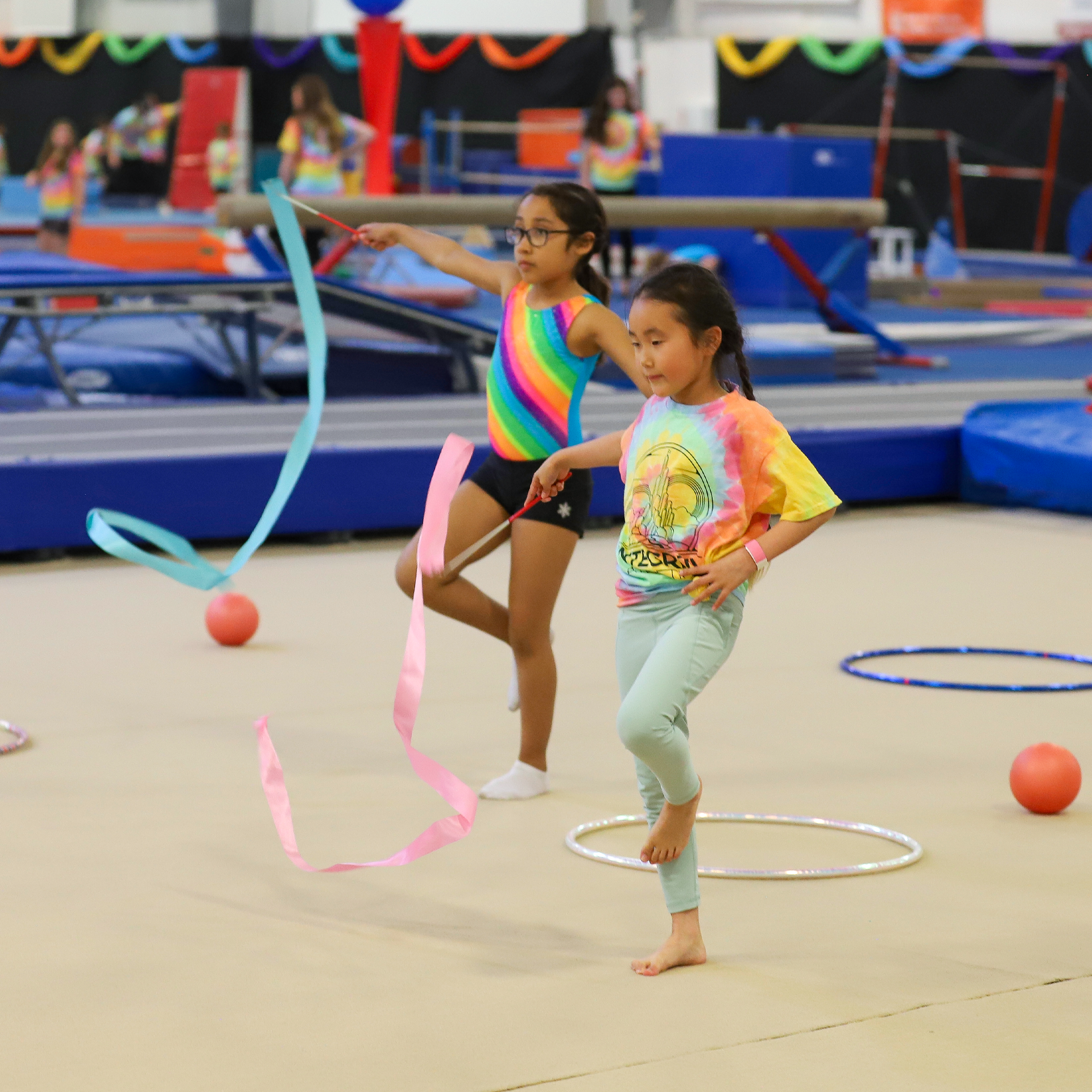 Two young girls are practicing rhythmic gymnastics in a gym