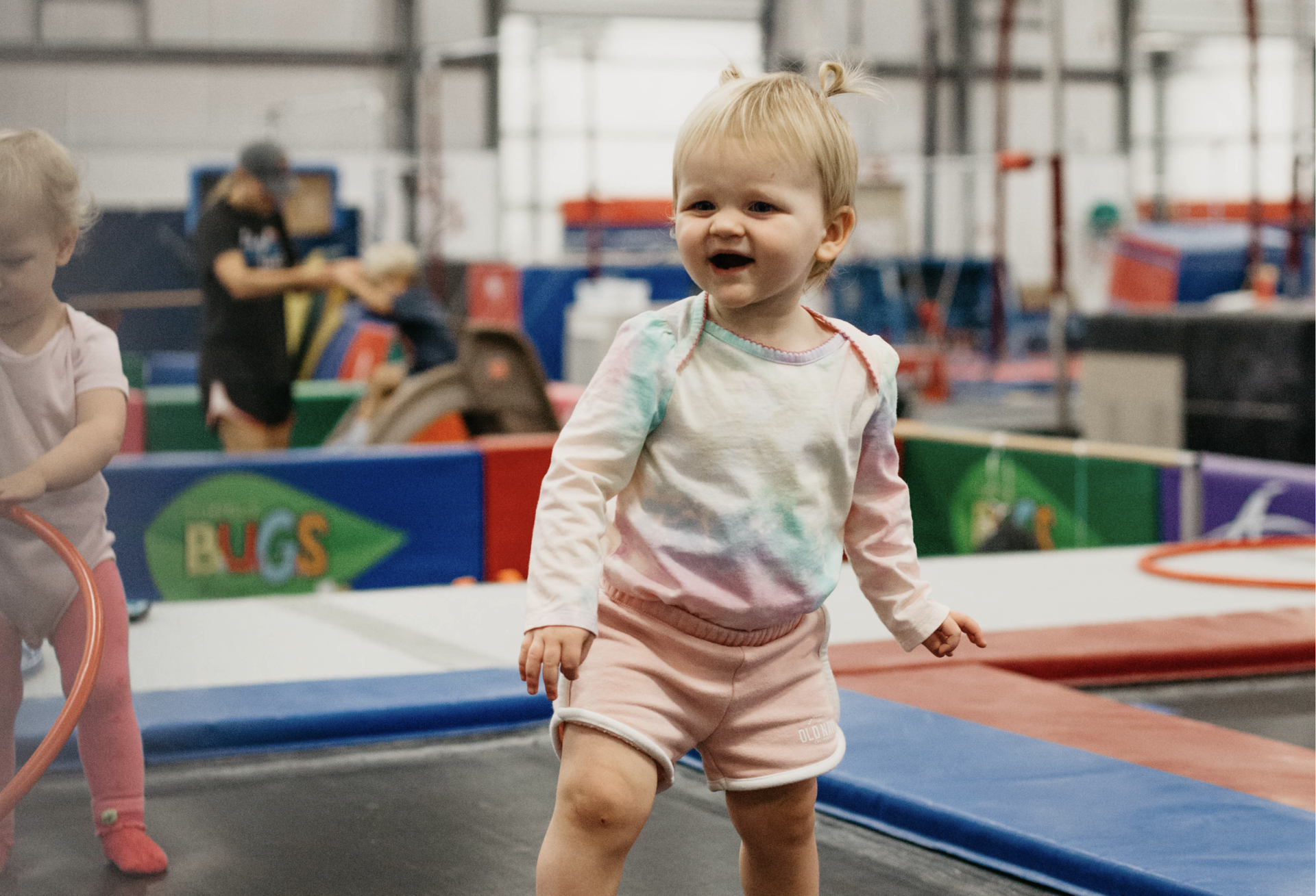 A little girl is standing on a trampoline in a gym.