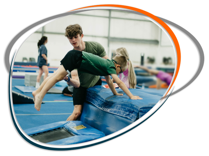 A man is helping a young boy do a handstand on a trampoline.