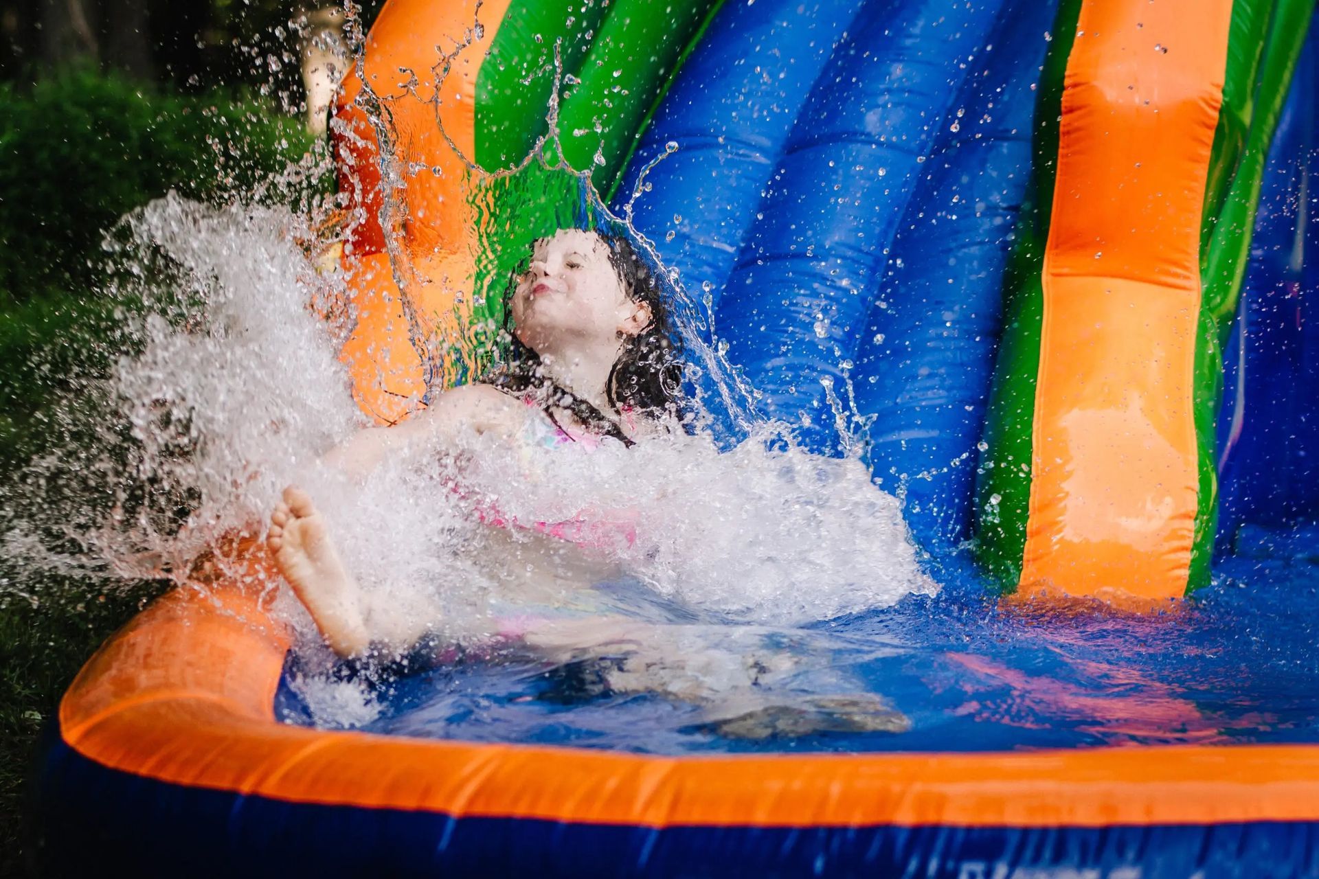 A young girl is sliding down a blue inflatable slide sponsored by integrity adventures summer camp