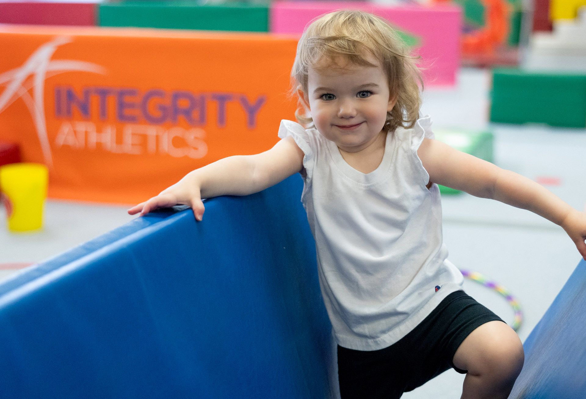A little girl is standing on a trampoline in a gym.