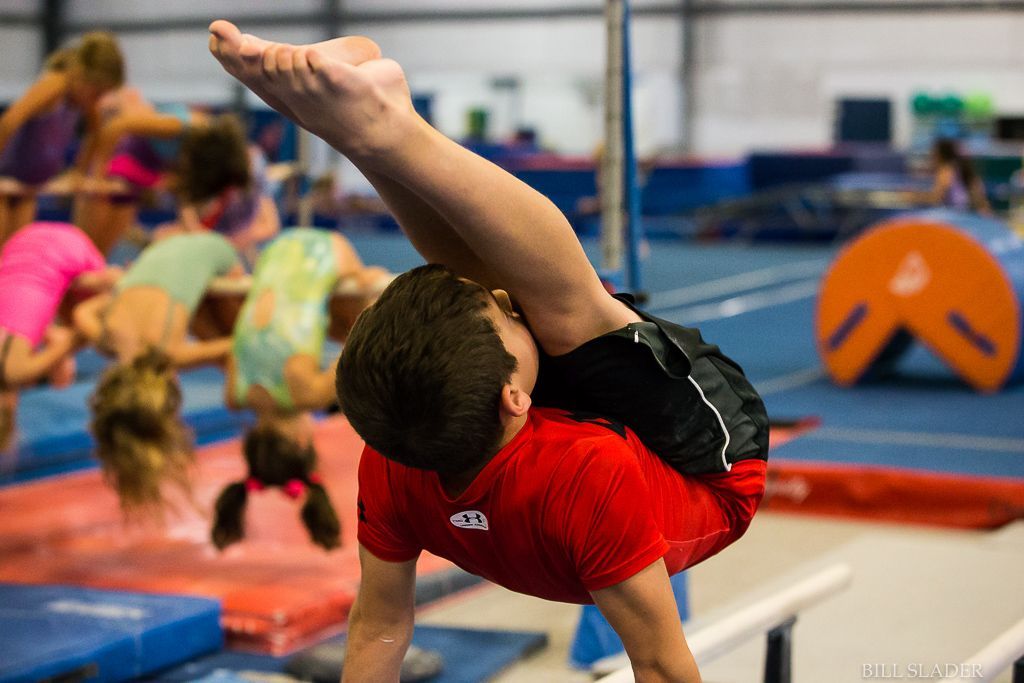 A young boy is doing a handstand on a balance beam in a gym.
