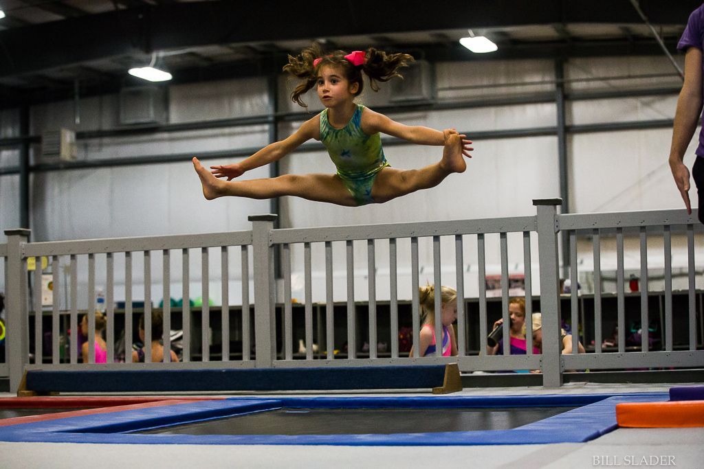 A little girl is doing a split on a trampoline.