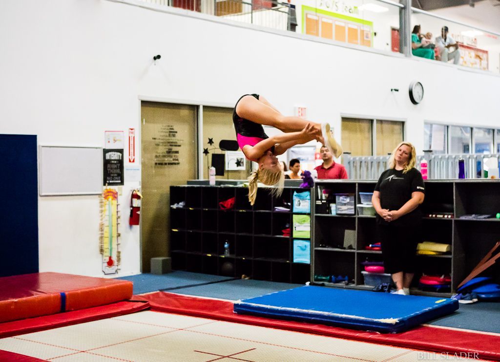 A girl is doing a flip on a trampoline in a gym.