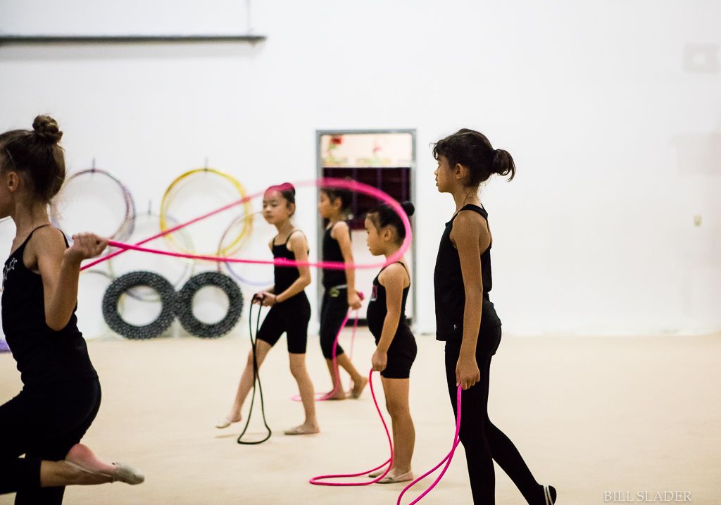 A group of young girls are practicing rhythmic gymnastics in a gym.