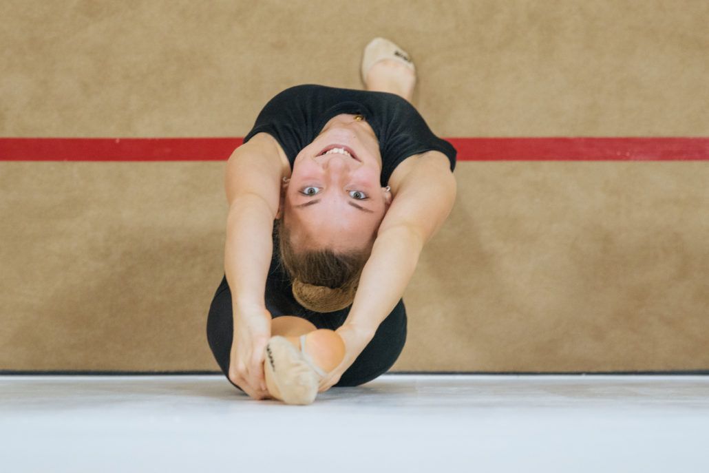 A female gymnast is doing a handstand on a balance beam.