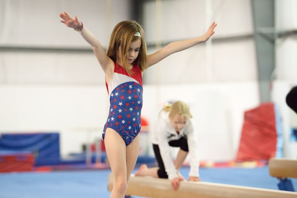 A young girl is standing on a balance beam in a gym.