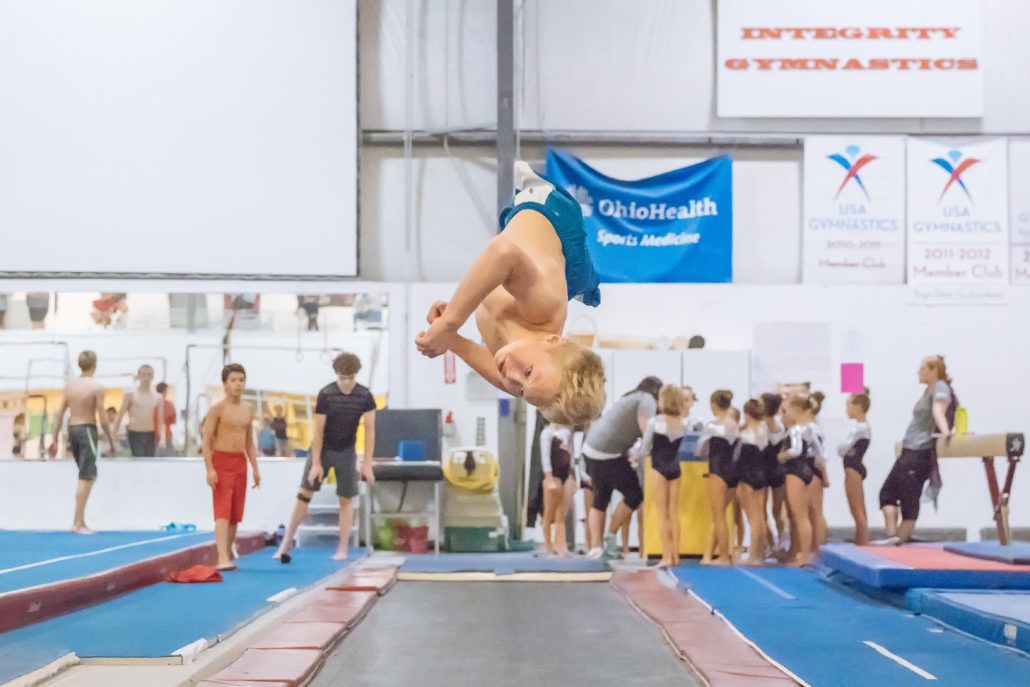 A boy is doing a flip on a trampoline in a gym.