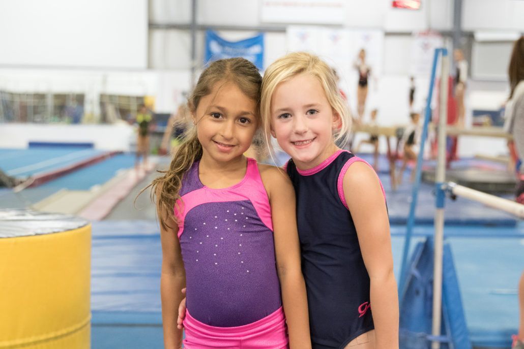 Two young girls are posing for a picture in a gym.