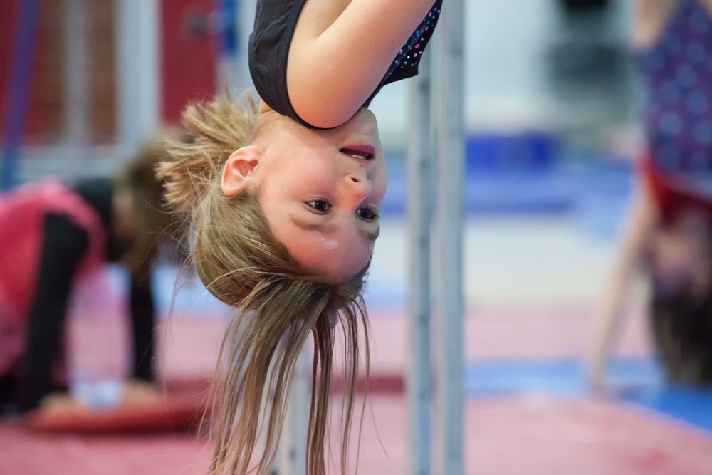 A young girl is doing a handstand on a bar in a gym.