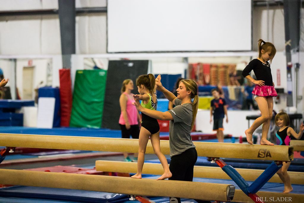 A woman is helping a young girl balance on a balance beam in a gym.