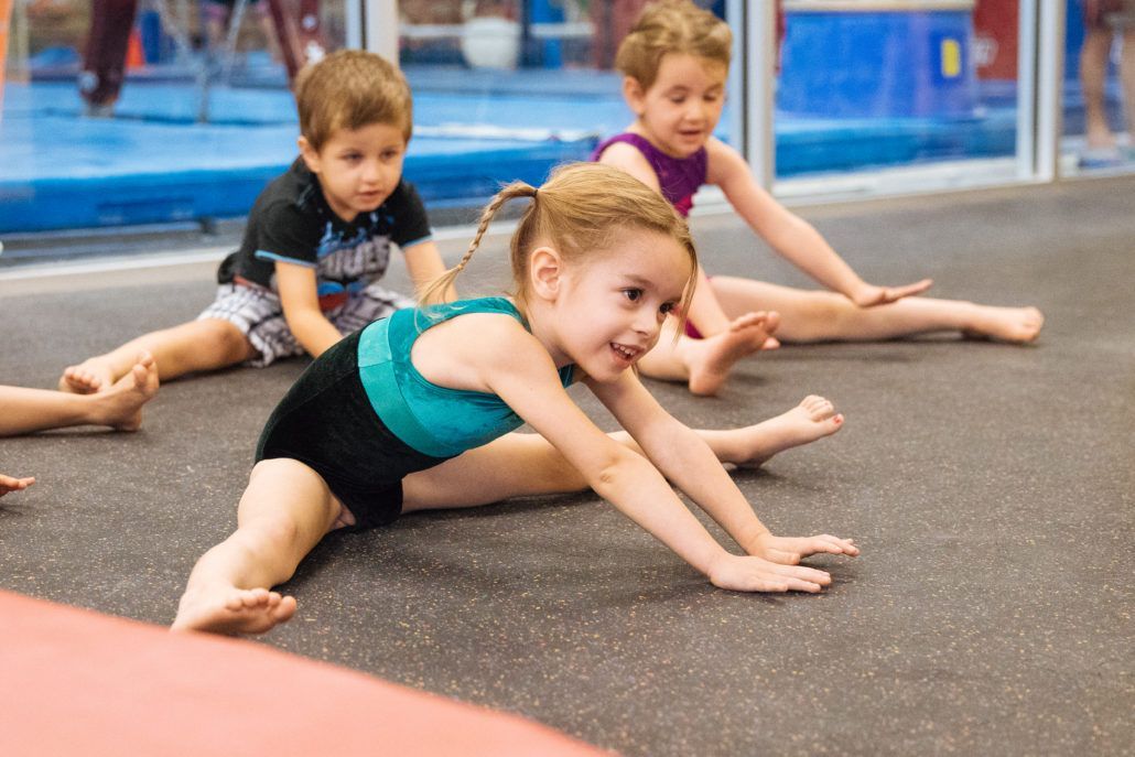 A group of young children are doing stretching exercises on the floor.