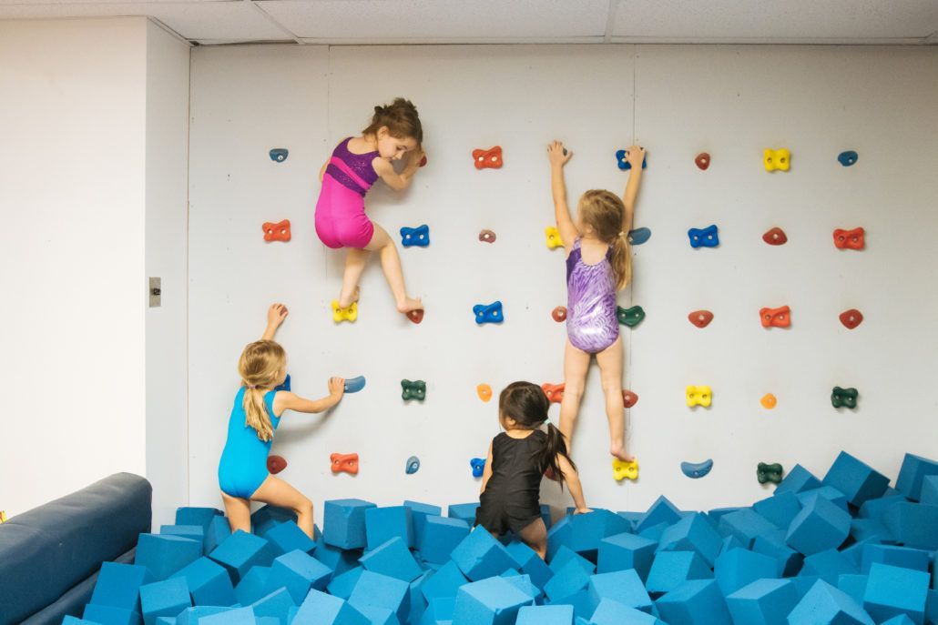 A group of children are climbing a climbing wall in a gym.