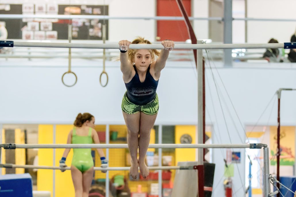 A young girl is doing a handstand on a bar in a gym.