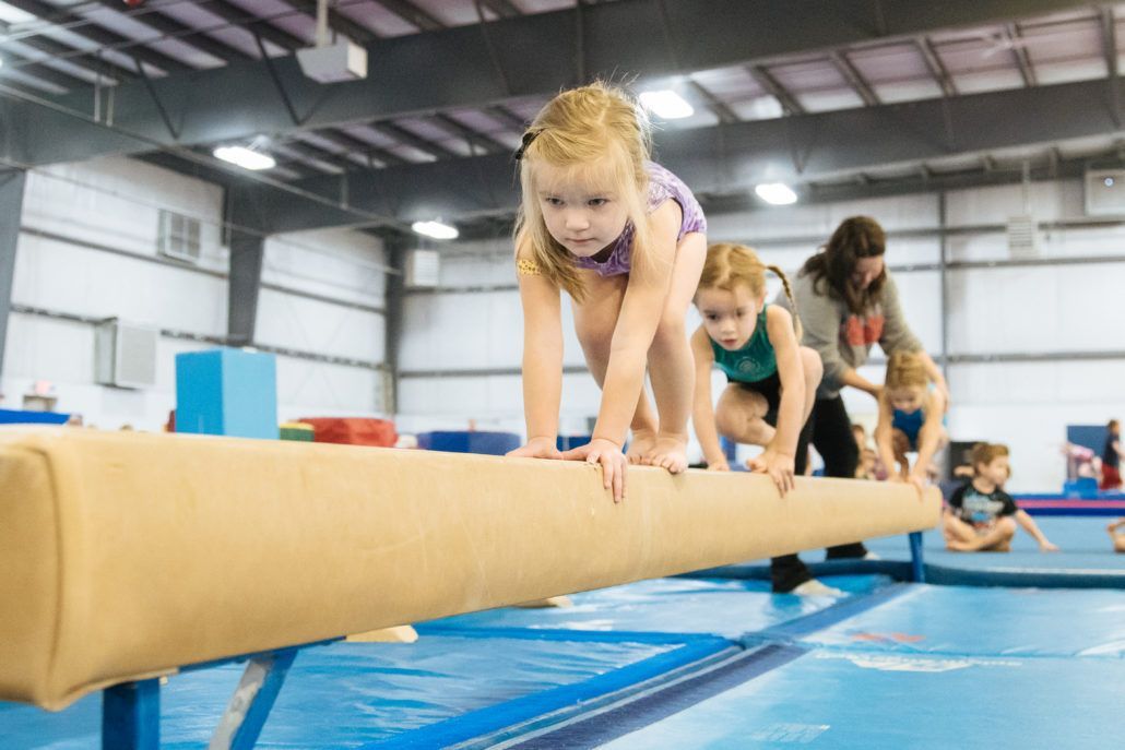 A little girl is climbing on a balance beam in a gym.