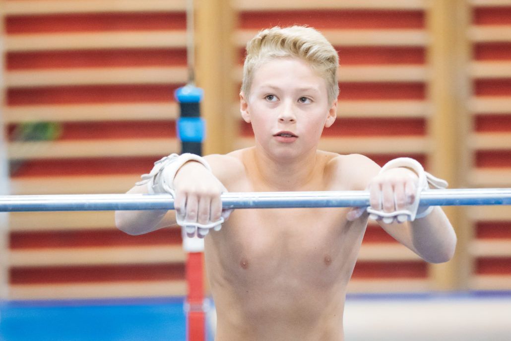 A young boy is doing exercises on a bar in a gym.