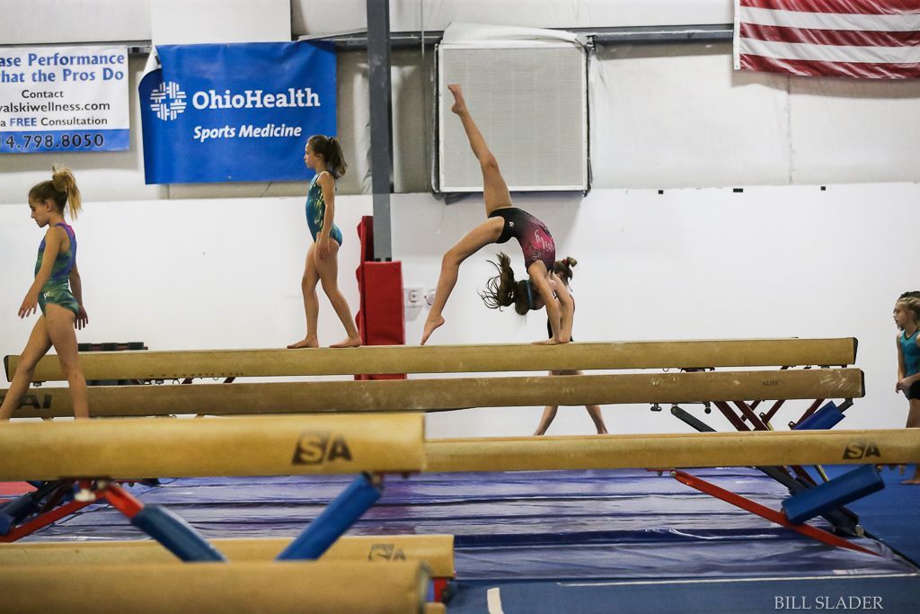 A girl is doing a handstand on a balance beam in a gym.