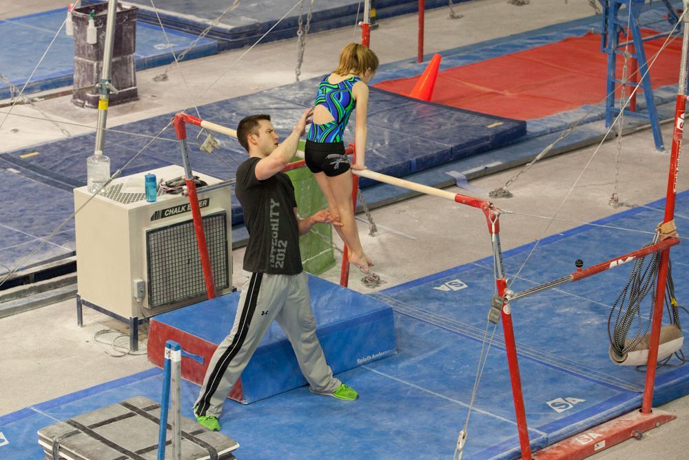 A man is helping a girl do a trick on a parallel bars.