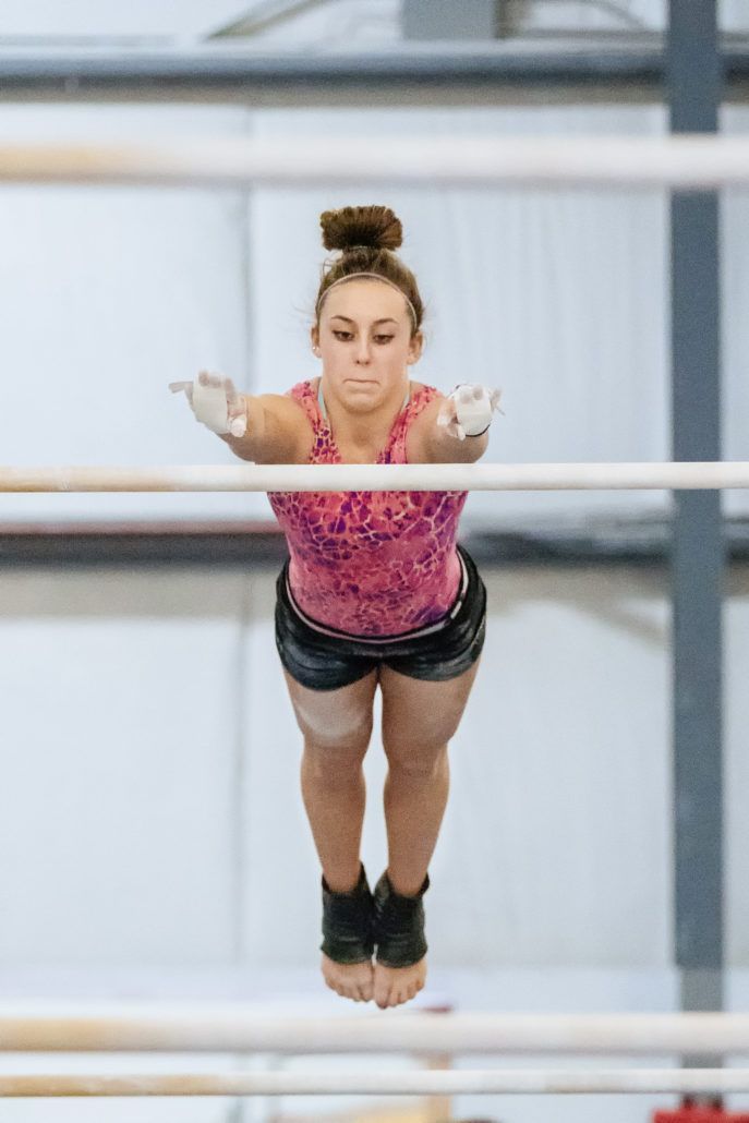A female gymnast is doing a trick on the parallel bars.