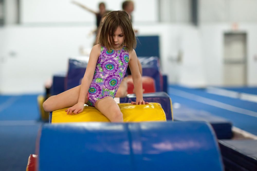 A little girl is sitting on a yellow block in a gym.