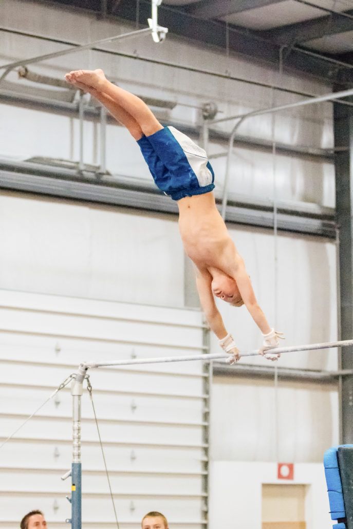 A young boy is doing a handstand on a parallel bars in a gym.