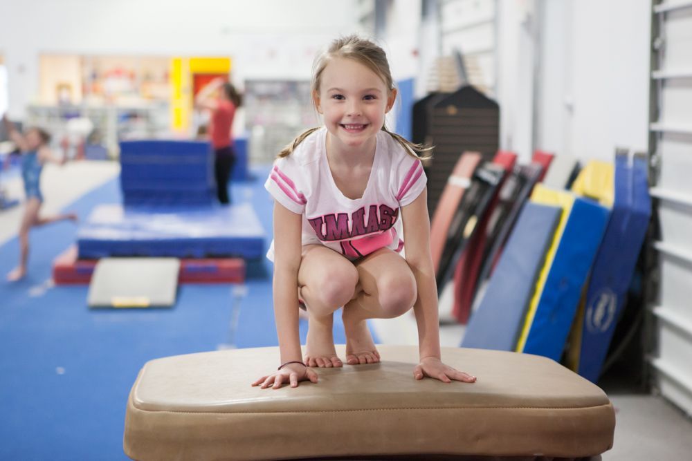 A young girl is squatting on a balance beam in a gym.