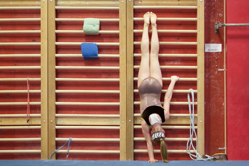 A woman is doing a handstand against a wall in a gym.