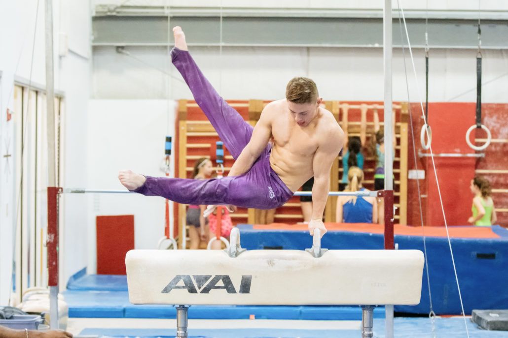 A man is doing a trick on a pommel horse in a gym.