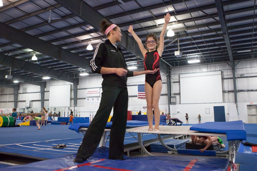 A woman is standing next to a young girl on a trampoline.
