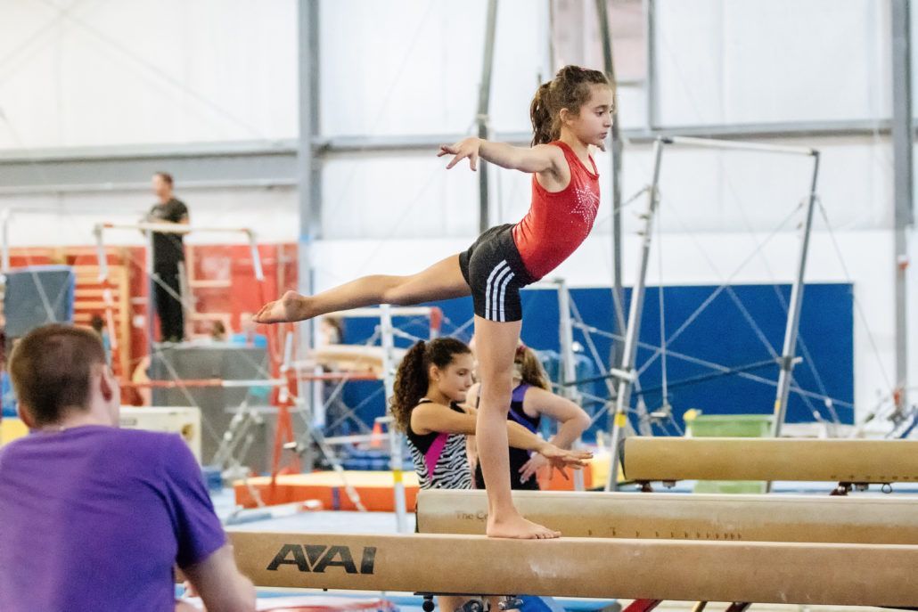 A girl is doing a balance beam in a gym while a man watches.