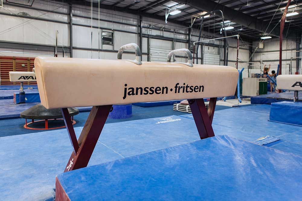 A janssen fritsen pommel horse is sitting on a blue mat in a gym.