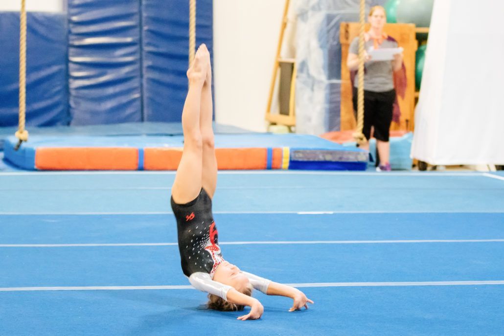 A gymnast is doing a handstand on a blue mat in a gym.