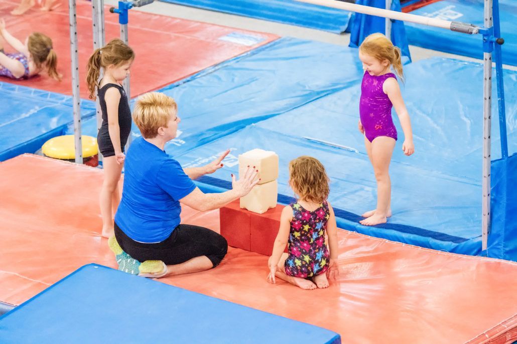 A woman is teaching a group of young girls how to do gymnastics in a gym.