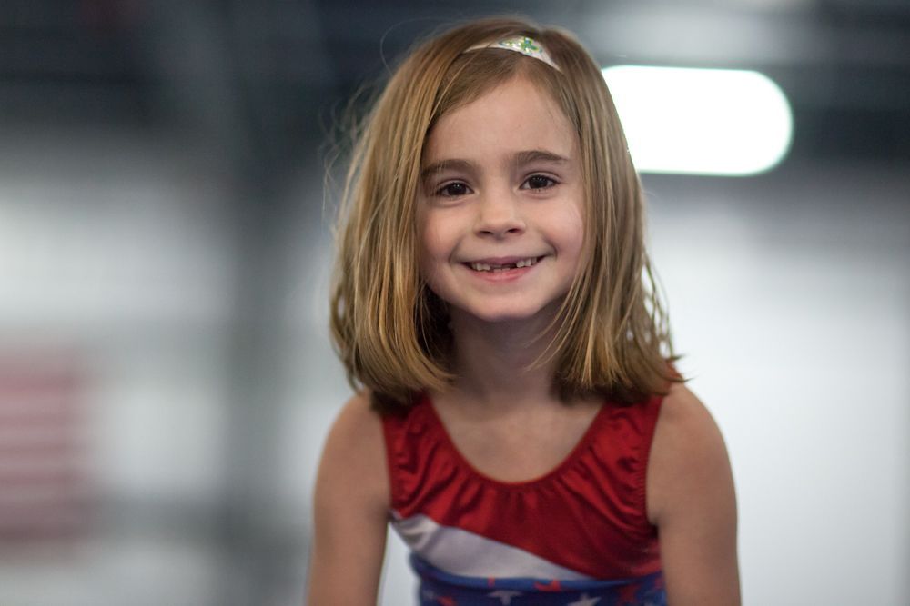 A little girl in a red and white leotard is smiling for the camera.