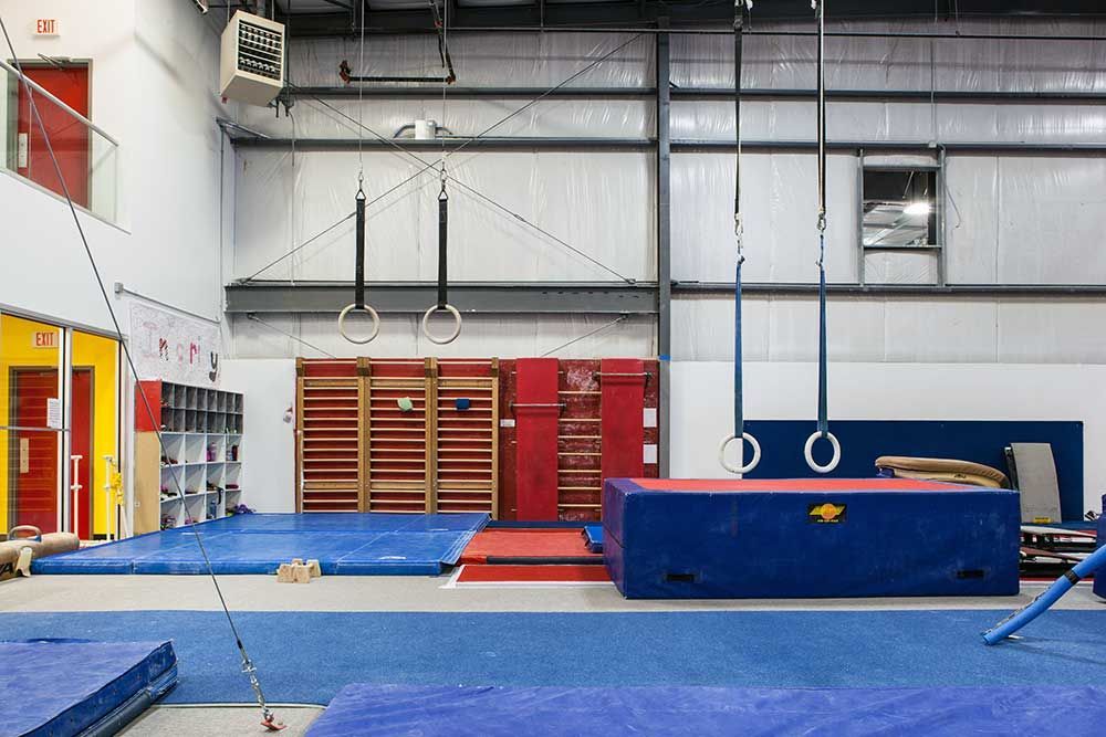 A gym with a blue mat , rings , and a balance beam.