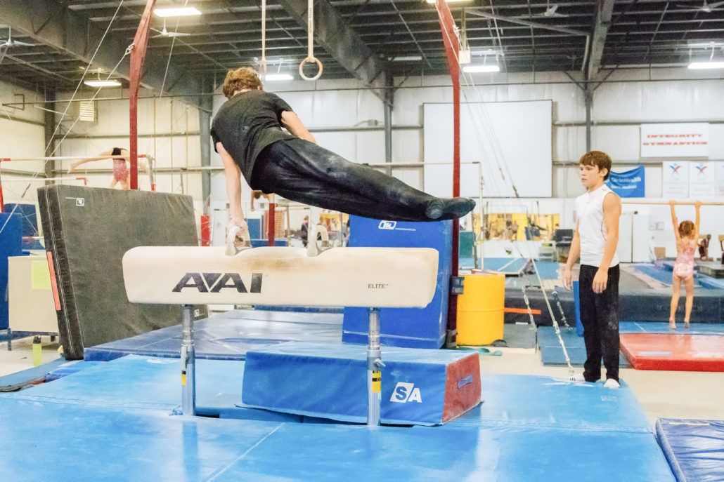 A man is doing a trick on a pommel horse in a gym.