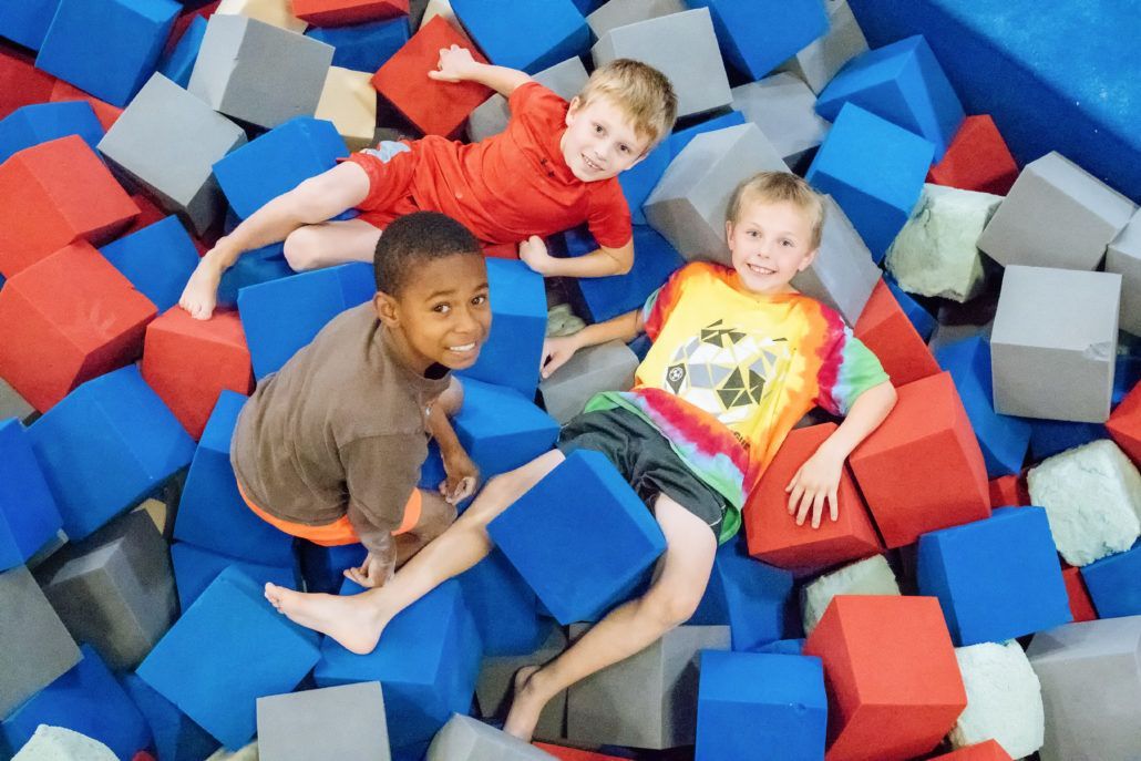 Three young boys are laying in a pile of foam cubes.