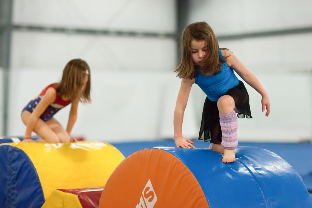 Two young girls are playing on a gym mat.