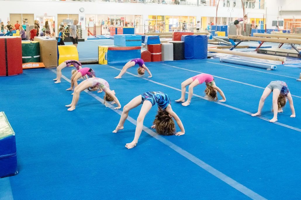 A group of young girls are doing gymnastics on a blue mat in a gym.