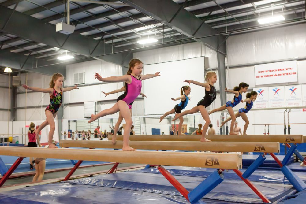 A group of young girls are doing gymnastics on balance beam in a gym.