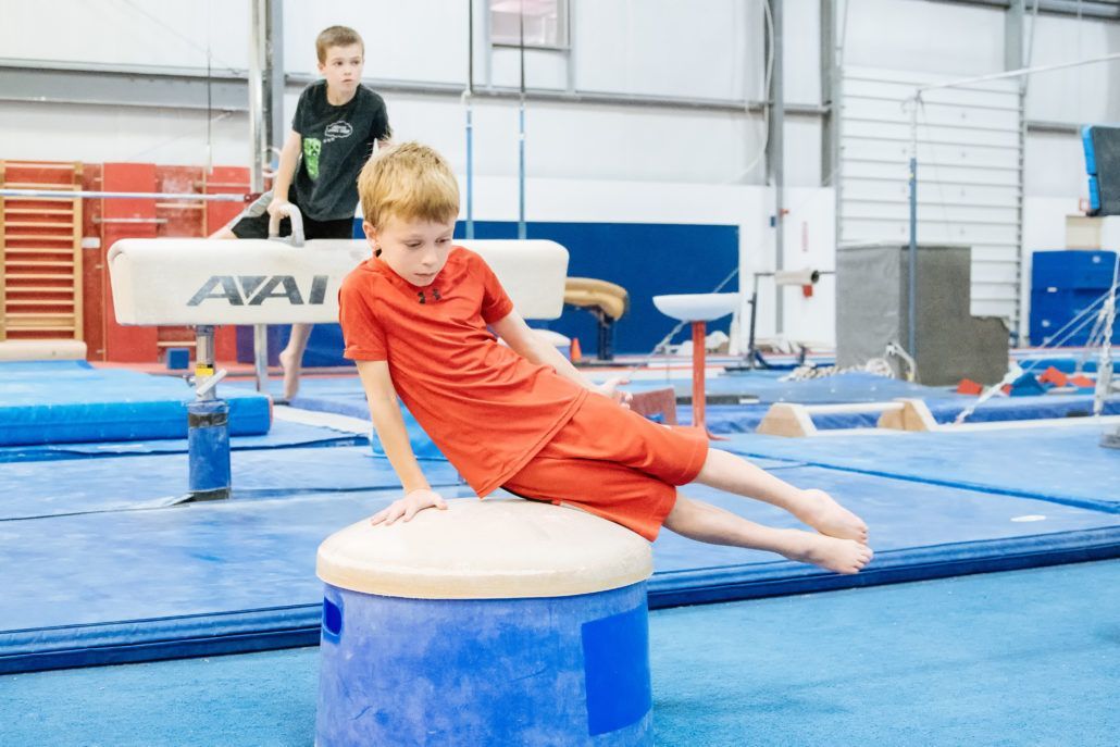 A young boy is doing a trick on a balance beam in a gym.