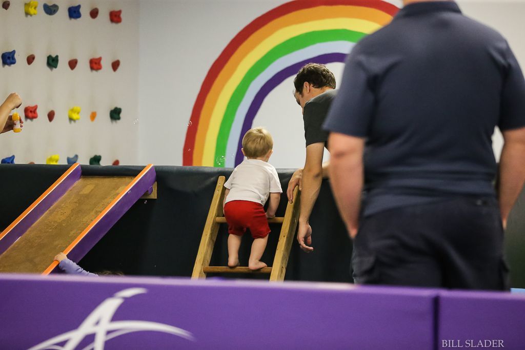A little boy is climbing up a wooden ladder in front of a rainbow.