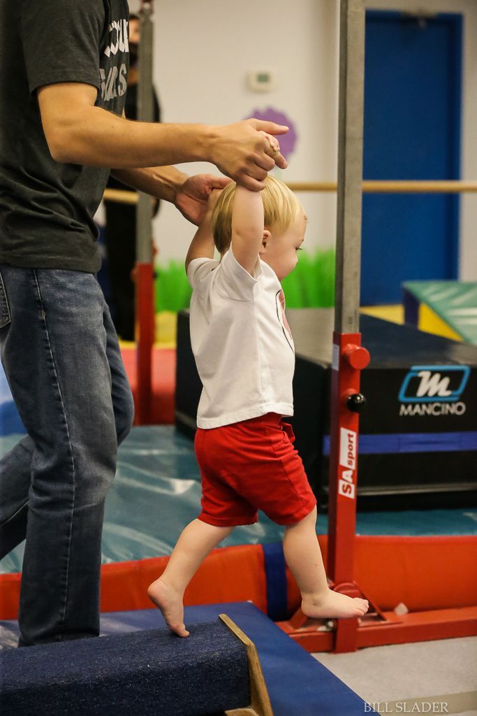 A man is helping a little boy walk on a balance beam.