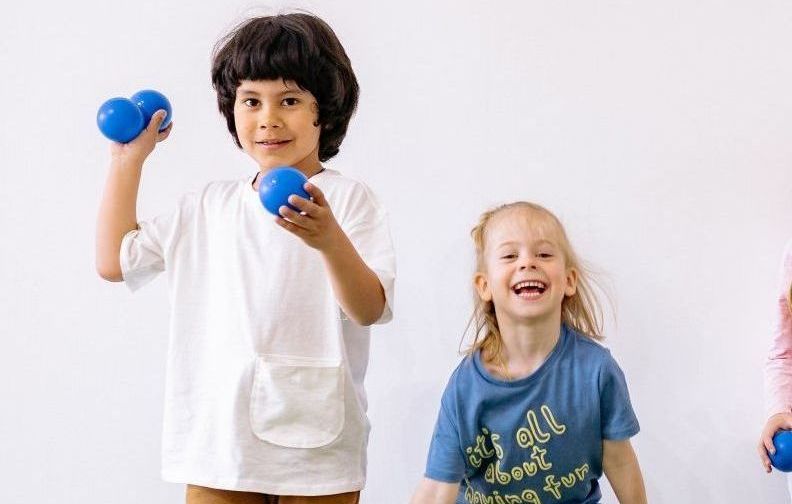 A boy and a girl are holding blue dumbbells in their hands.