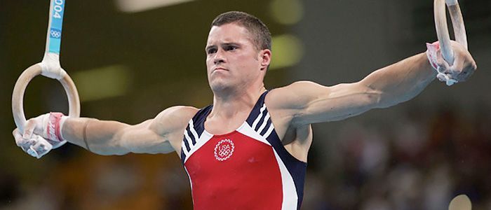 A male gymnast is doing exercises on rings with his arms outstretched.