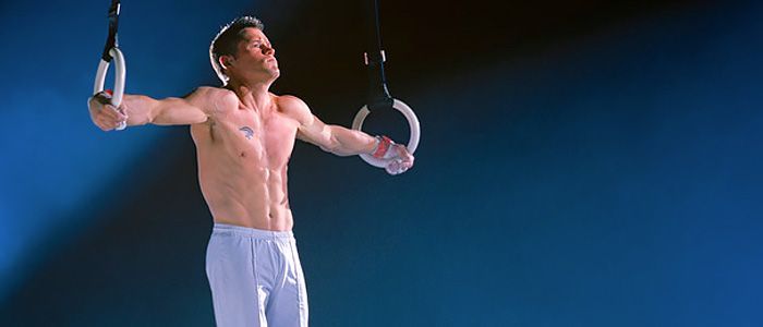 A shirtless man is holding gymnastic rings in his hands.